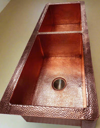 Detailed close-up of the hammered texture on the double-bowl copper kitchen sink with apron, highlighting the unique and artisanal finish.