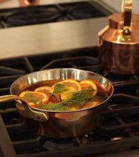 Close-up of the double-layered copper and stainless steel Windsor warming pan with food, highlighting even heat distribution for perfect warming.
