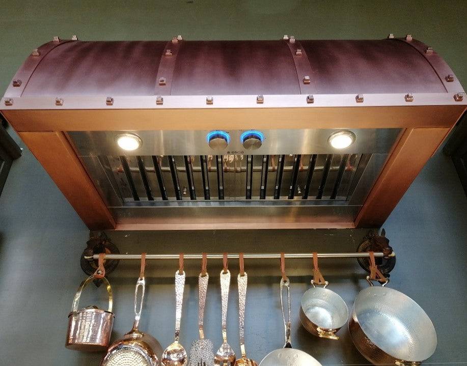 Amoretti Brothers WINSTON copper range hood, handcrafted solid copper with rivets, above stove with hanging cookware.