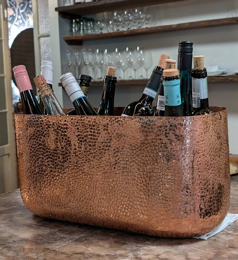 Oval hammered copper ice bucket with ice and beverages inside, showcasing its elegant design