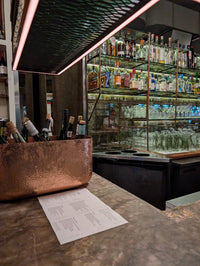 Full view of the oval hammered copper ice bucket on a bar counter, demonstrating its size and style.