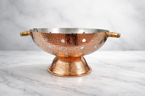 Copper colander on a marble surface with a white background