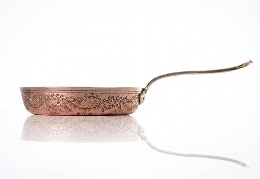 Copper frying pan with floral patterns on a white background