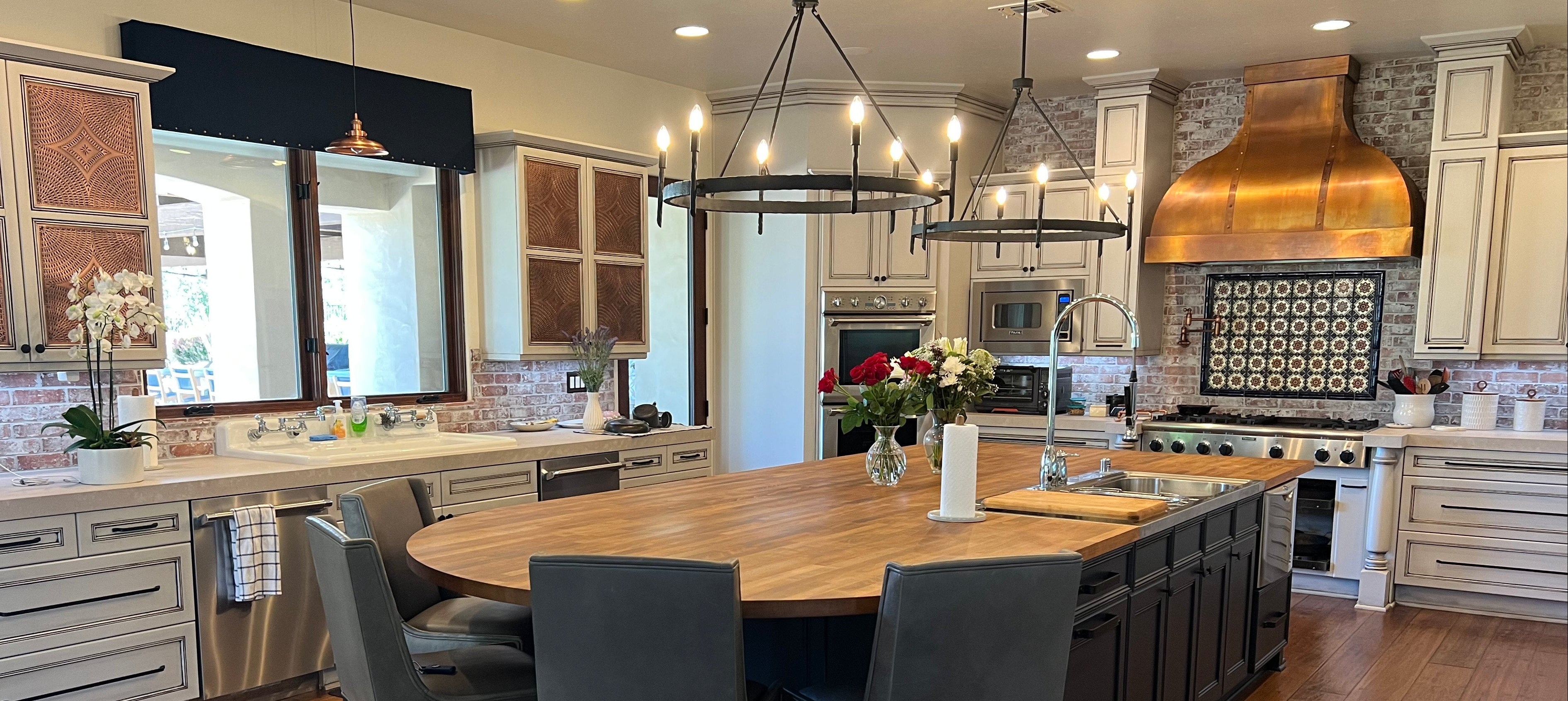 Modern kitchen with wooden dining table and chairs, stainless steel appliances, and copper hood.