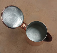 Copper teapot with textured interior on a beige surface