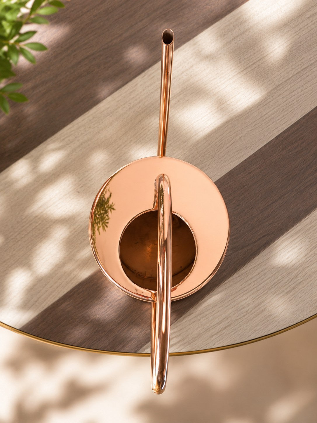 Copper watering can on a wooden surface with natural light casting shadows.