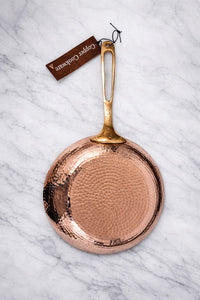 Hammered copper frying pan by Amoretti Brothers with gold handle on a marble surface 