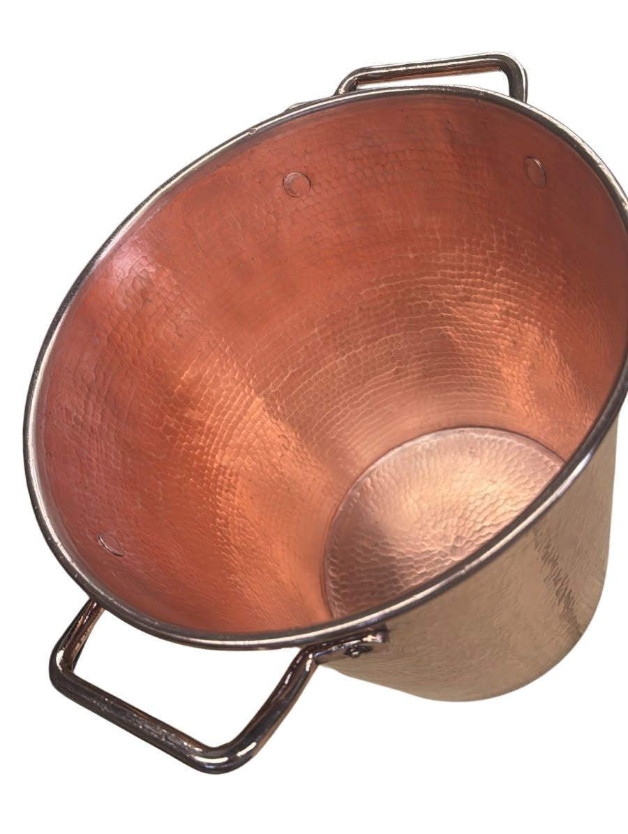 A hammered copper bucket with a polished copper interior and dark metal side handles, shown on a plain white background.