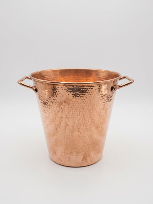 A hammered copper bucket with two side handles, photographed on a clean light gray studio background.