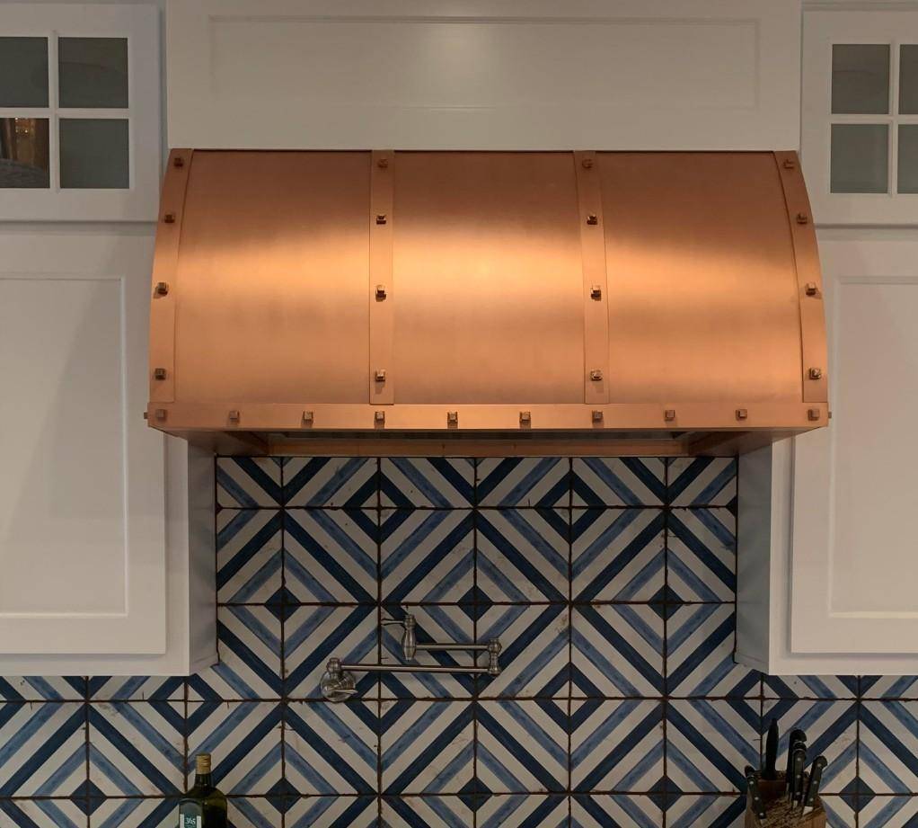 Handcrafted Amoretti Brothers WINSTON Copper Range Hood over blue geometric tile backsplash.