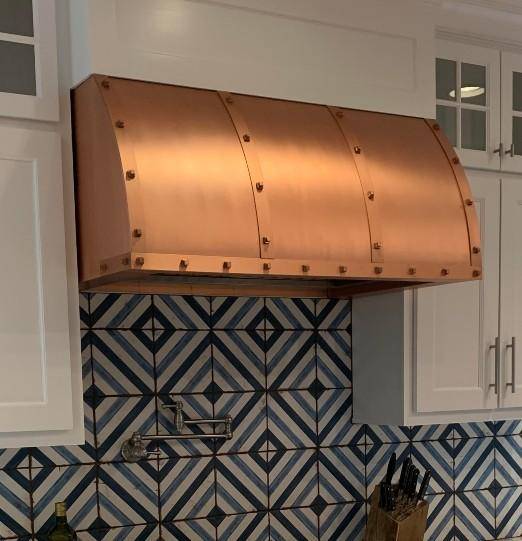 Amoretti Brothers WINSTON handcrafted copper range hood over geometric blue tile backsplash.